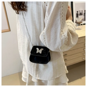 Close-up of black velvet mini crossbody bag with silver butterfly clasp on white dress