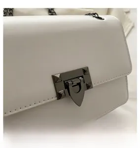 Detail of dark gunmetal lock with pyramid studs on a white leather shoulder bag