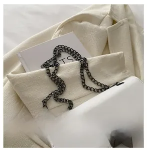 Close-up of white crossbody bag featuring metallic chain and pyramid stud clasp details