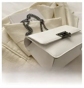 Detailed view of white leather chain bag with dark metal buckle on cream background