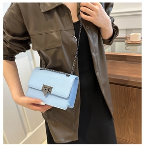 Detail of light blue leather crossbody bag with metal chain strap and lock buckle