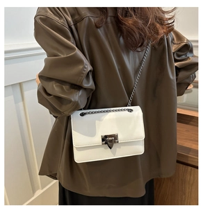 Detailed shoulder view of a white leather chain bag with metallic clasp on model