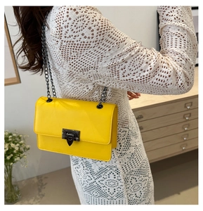 Detail of bright yellow glossy chain bag with metal clasp worn by a model