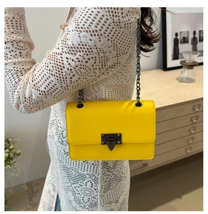 Detail of yellow crossbody bag with V-shaped metal lock and rivet decor on model