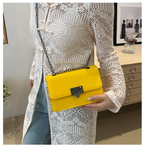 Detail of bright yellow PU leather crossbody bag with black matte chain and triangular lock