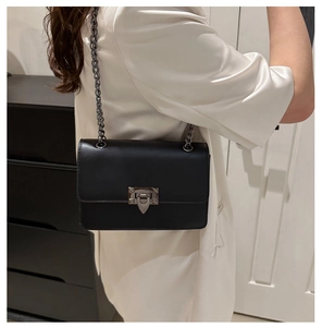 Close-up of minimalist black crossbody bag with metal chain strap on model in indoor setting