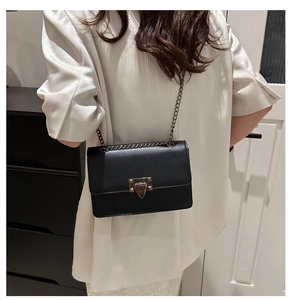 Detail of minimalist black crossbody bag with silver metal chain and lock on model