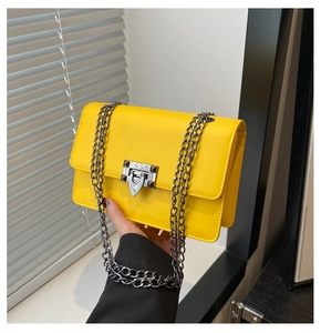 Detail of a bright yellow chain crossbody bag with a square metal lock and rivet elements
