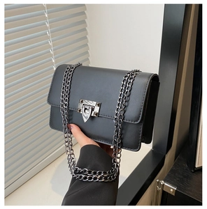 Detail of black faux leather crossbody bag with metal shield buckle and studded chain strap