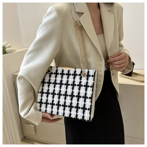 Detail of black and white tweed tote bag with gold chain strap on model's shoulder
