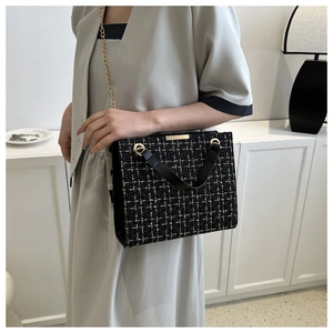 Detail of black tweed crossbody bag with gold chain strap and metallic buckle