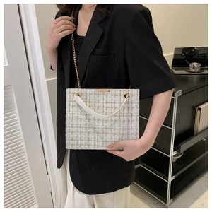 Close-up of white tweed shoulder bag with gold chain strap on a black blazer outfit