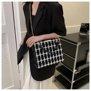 Detailed close-up of a black and white tweed plaid handbag with golden chain strap and leather handle