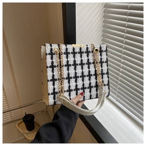 Detail of tweed shoulder bag with golden chain strap and metallic clasp on a white surface