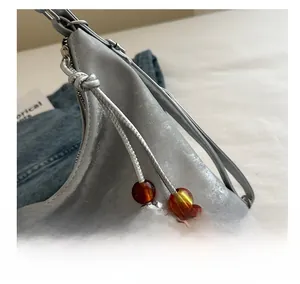 Detailed close-up of a silver crescent handbag featuring orange bead accents and metal zipper