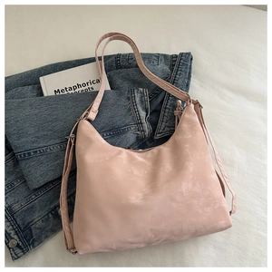 Detailed view of pink suede dumpling bag with curved silhouette on white fabric