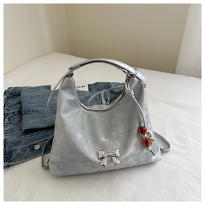 Detail of silver metallic handbag with bow buckle and beaded tassel on denim background