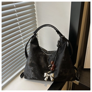 Detail of black washed hobo bag with metallic bow and bead charms on window sill