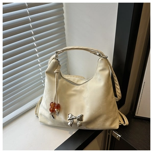 Detail of a creamy beige crescent bag with a silver metallic bow and bead tassel accent
