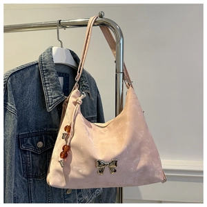 Detail of pink shoulder bag featuring a metallic bow and beaded pendant on denim backdrop