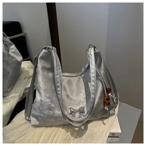 Detail of silver textured shoulder bag with metallic bow and beaded charm on mirror