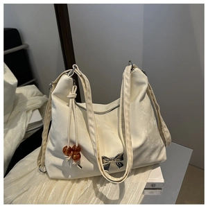 Detail of cream shoulder bag with silver bow accent and amber bead charm on fabric
