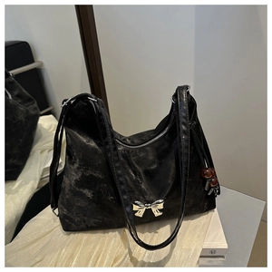 Detail of black velvet shoulder bag with silver bow hardware and red bead tassel