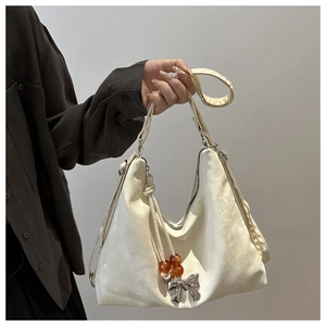 Detail of cream white shoulder bag featuring a velvet texture and metallic bow pendant