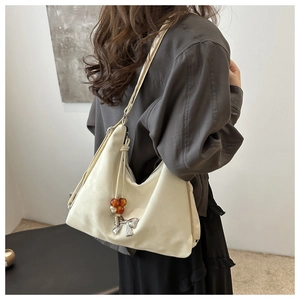 Close-up of cream crossbody bag with metal bow and amber bead details on a model