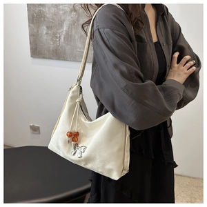 Detail of white satin shoulder bag featuring silver bow pendant and beaded charm decoration
