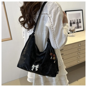 Detail of black velvet shoulder bag with silver bow and amber bead charm on a model