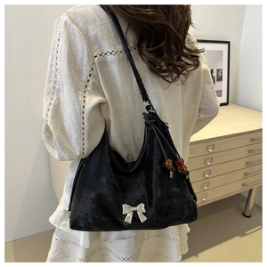Detail of black tote bag with silver bow and amber beads worn by a model in soft lighting