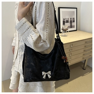 Detail of black crossbody bag with silver metal bow and amber bead charm on white dress