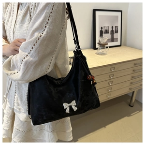 Detail of a black glossy shoulder bag featuring a 3D silver metal bow and beaded charm