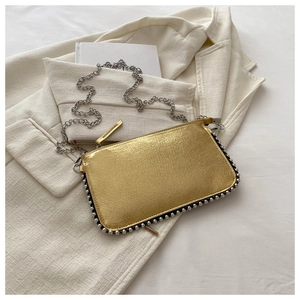 Detailed close-up of metallic gold crossbody bag with silver beaded trim on beige blazer