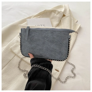 Detail of grey suede envelope bag with silver studs and chain strap held by a person