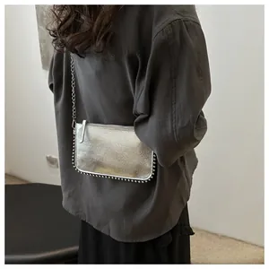 Detail of silver metallic chain bag with rivet trim worn by a model in casual outfit