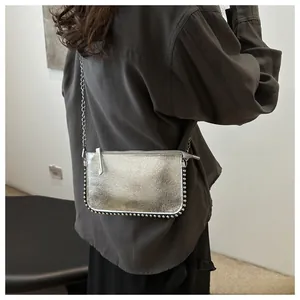 Detail of silver crossbody bag with bead trim and chain strap shown on a model