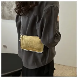 Detail of gold metallic crossbody bag with silver bead trim and chain strap on a model