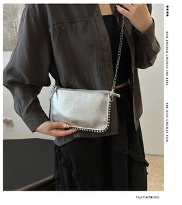 Detail of silver metallic bag with rivet edges and chain strap shown in mirror reflection