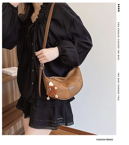 Detail of a brown crescent shoulder bag in vintage oiled leather with a plush charm