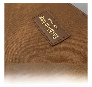 Detail of a brown canvas bag featuring a stitched faux leather label with gold lettering