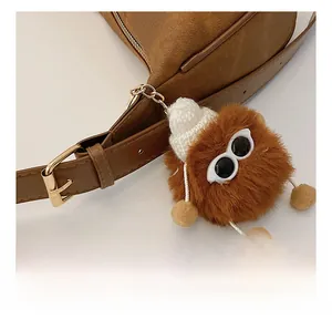 Detail of brown plush monster charm with white knit hat on leather shoulder bag
