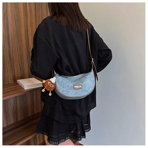 Detail of light blue crescent bag with brown leather trim and plush bear charm