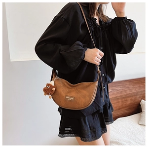 Detail of a brown half-moon bag featuring a plush monster charm and leather patch