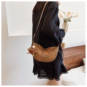 Detail view of brown dumpling shoulder bag with plush charm and branded leather patch