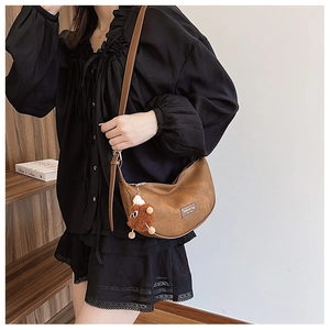 Detailed shot of brown vintage crescent bag featuring textured leather and plush charm