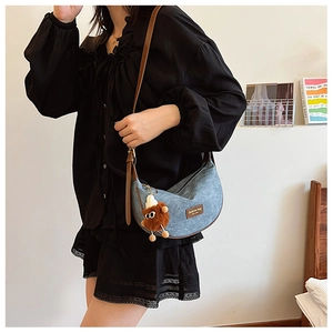Detail of blue denim crescent bag featuring brown leather tag and quirky plush charm