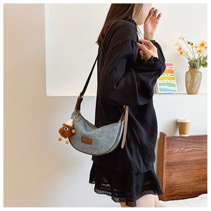 Detail of blue denim crescent bag with leather patch and brown plush eye charm