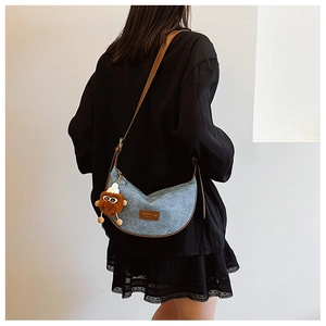 Detail of blue denim dumpling bag with brown leather strap and stylish plush pendant